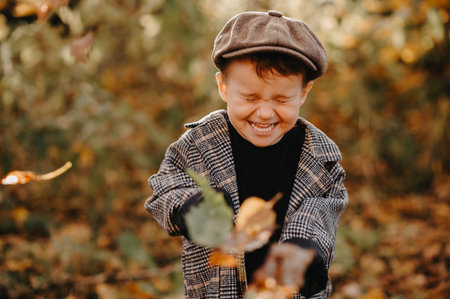 A happy baby boy is playing with yellow leaves in the golden autumn season in the park.の写真素材