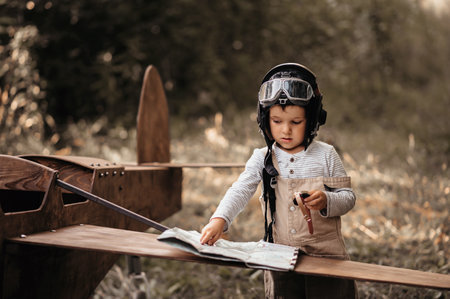 A young aviator boy near a homemade airplane in a natural landscape with a compass and a geographical map. The authentic mood of the picture. Cartography. Vintage.の写真素材