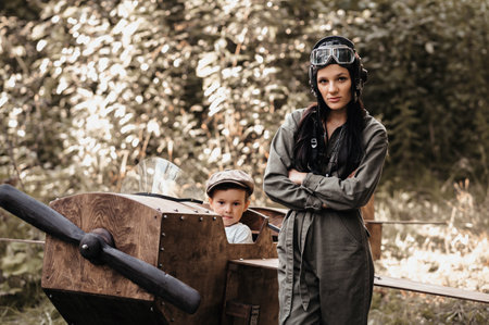 A young aviator boy sits in a homemade airplane in a natural landscape. Next to her is an aviator mom in a helmet and glasses. The authentic mood of the picture. . Cartography. Vintage.の写真素材