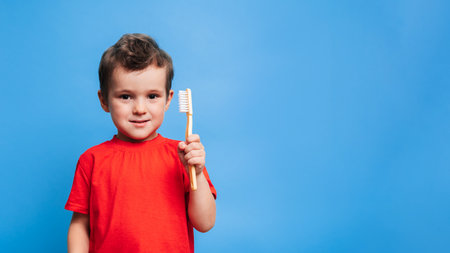 A smiling boy with healthy teeth holds a toothbrush on a blue isolated background. Oral hygiene. A place for your text.の写真素材