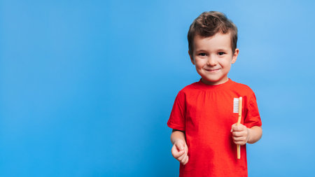 A smiling boy with healthy teeth holds a toothbrush on a blue isolated background. Oral hygiene. A place for your text.の写真素材