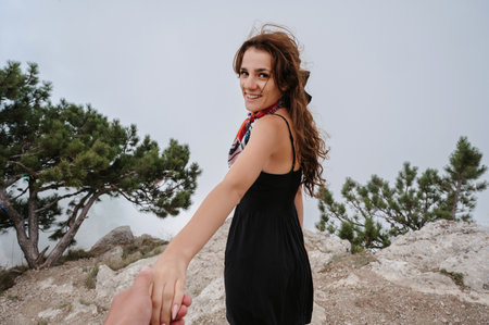 A brave woman guiding a traveler by the hand into a wild rocky terrain. Mountain landscape under the skyの写真素材