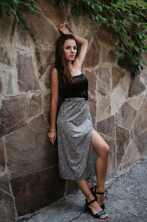 A young brunette poses against a stone wall with green ivy. A beautiful and slender figure. A girl in a dress.の写真素材