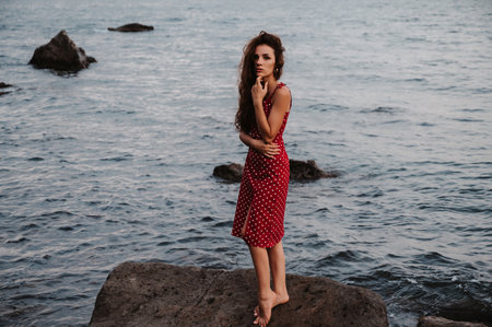 A dramatic portrait of a young attractive woman standing on a large boulder in the middle of the sea.の写真素材