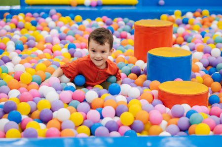 A happy little boy has fun jumping into a dry pool with colorful balls. The kid boy is playing and having a good time in the game room with colorful balls.の写真素材