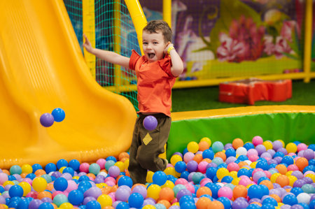 A happy little boy has fun jumping into a dry pool with colorful balls. The kid boy is playing and having a good time in the game room with colorful balls.の写真素材