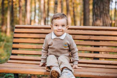 Happy boy sitting on a bench in the Park in autumnの写真素材