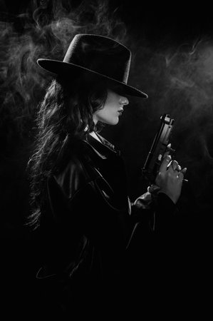 Silhouette: a female detective in a coat and hat with a gun in her hands. Dramatic noir portrait in the style of books and detective films of the 1950s. black and white snapshotの写真素材