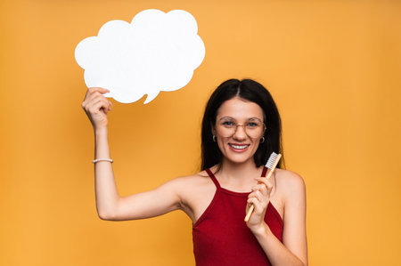 A smiling woman with healthy teeth is holding a toothbrush and a clean empty banner. A young beautiful girl on a bright isolated background. Oral hygiene. A place for your text.の写真素材