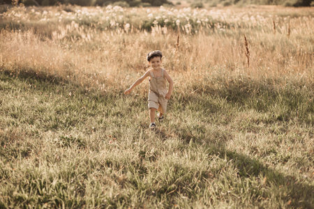 The boy-child is having fun and actively running in the field. A cheerful and sincerely rejoicing boy. Childhood in the countryside.の写真素材