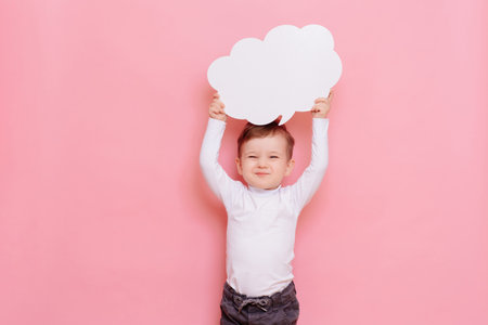 studio portrait of a happy boy with a clean white board in the shape of a cloudの写真素材