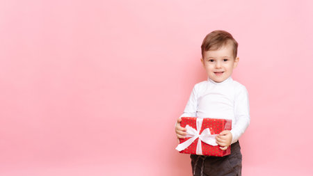 Gift in Hands Boy. Happy Baby Boy with Gift Box in Hands isolated on pink background.の写真素材