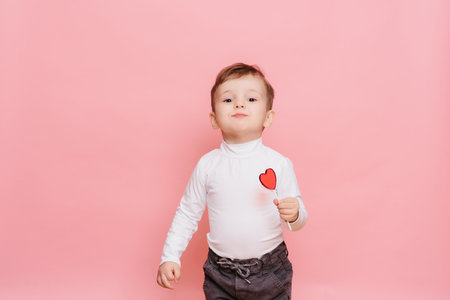 studio portrait of a little boy with a heart-shaped lollipop in his hand.の写真素材