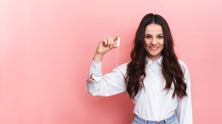 A young woman holds a menstrual swab in her hands. Pink background. Space for text. The concept of feminine hygiene.の写真素材