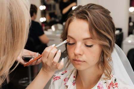 Shooting in a beauty salon. makeup artist applies makeup to a young beautiful girl bride.の写真素材