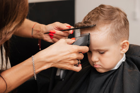 Shooting in a beauty salon. A barber makes a haircut for a little boy with a machineの写真素材