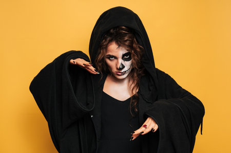 A young woman in a hood with scary makeup. on a yellow isolated background. Concert costume party. Banner.の写真素材