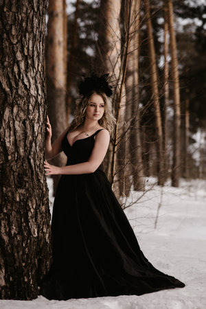 Portrait of a young girl in the image of a dark witch standing by a tree in the middle of the forest. An image for Halloween. Mysticismの写真素材