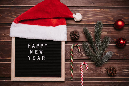Happy New Year inscription on a letter board in New Year decorations, Santa hat, fir branches,...