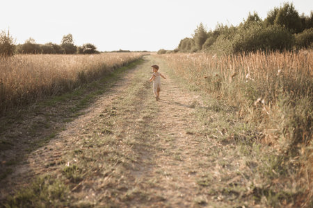 The boy-child is having fun and actively running in the field. A sincere and joyful boy. Childhood in the countryside.の写真素材