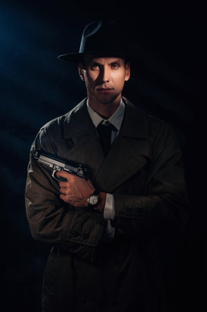 Silhouette of a male detective in a coat and hat with a gun in his hands. A book drama noir portrait in the style of detectives of the 1950s.の写真素材