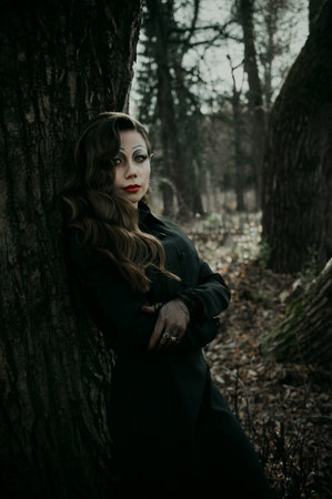 A young woman in a Gothic gloomy image of a witch in a forest surrounded by smoke. Halloween costume. Vertical photo.の写真素材