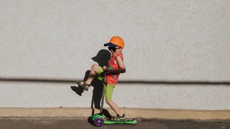 A little boy rides a scooter highlighted on a light wall. Open air. Minimalism. Panoramic banner.の写真素材