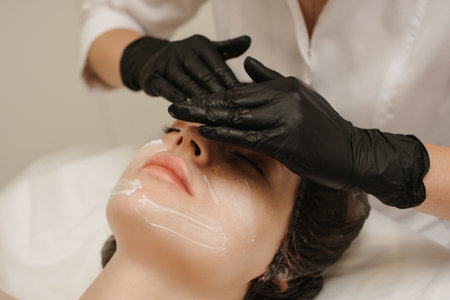 Close-up of the beauticians hands applying cream to the clients face and doing a massage. Facial skin care.の写真素材