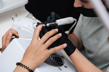 Hardware manicure. Close-up of a manicure master filing gel polish with a nail grinder with a cutter.の写真素材