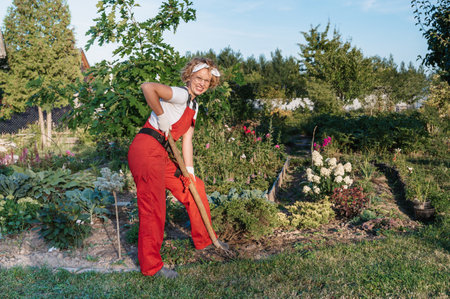 A happy female gardener in gloves and an apron stands against in a home garden . Gardening and...