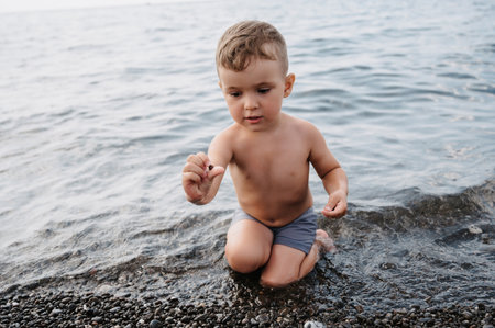 A cute boy is relaxing on the beach, playing with sea pebbles. Outdoor activities on the seashoreの写真素材