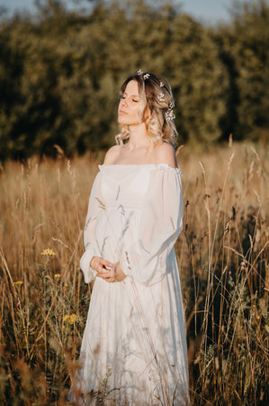 A young expectant mother in the third trimester of pregnancy in a white dress against the background of a natural landscape. The concept of future motherhood.の写真素材