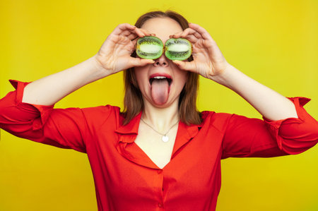 Portrait of a Caucasian girl with a radiant clean skin holding kiwi halves isolated on a yellow background. The concept of cosmetics with vitamins.の写真素材