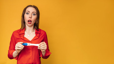 Studio shot of an emotional young woman with a positive pregnancy test in her hands. An expression of bewilderment on his face. The concept of pregnancy, motherhood. A place for your text.の写真素材