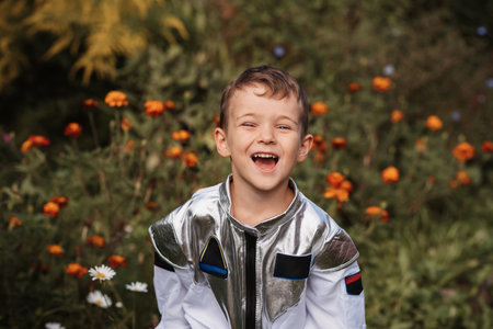A little boy in an astronaut costume plays outside surrounded by flowers on a sunny dayの写真素材