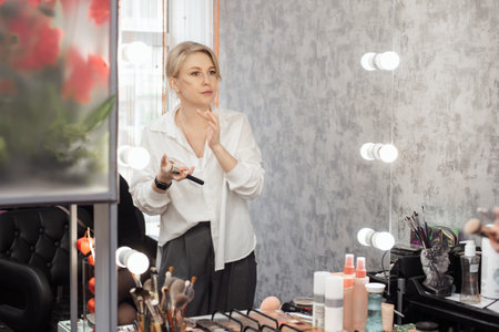 A young woman applies makeup in a home bathroom. She looks at herself in the mirror while powdering her faceの写真素材