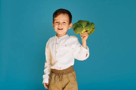 A studio shot of a boy holding fresh broccoli on a blue background. The concept of healthy baby food.の写真素材