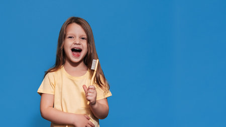 A smiling girl with healthy teeth holds a toothbrush in her hands on a yellow isolated background. A place for your text. Oral hygiene. Pediatric dentistry. Prosthetics. Rules for brushing teeth.の写真素材