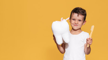 A smiling boy with healthy snow-white teeth holds a toothbrush and a plush tooth in his hands. A place for the text.の写真素材
