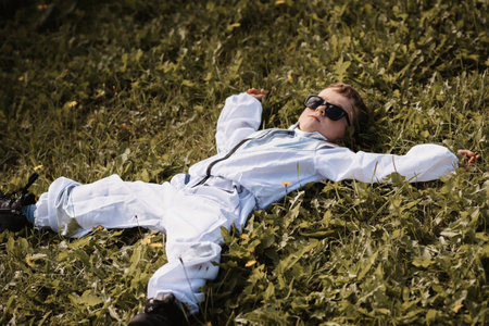 A little boy in an astronaut costume is playing outside lying on a field on a sunny dayの写真素材