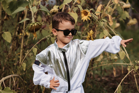 A little boy in an astronaut costume plays outside surrounded by flowers on a sunny dayの写真素材
