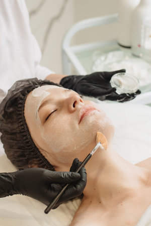 Facial peeling, spa treatments, skin care. A woman receiving facial care from a cosmetologist at a spa, close-up. Vertical photo.の写真素材
