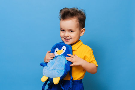 Cute little one cuddles with his backpack on a blue background. Funny kidの写真素材