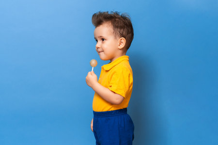 Baby boy with lollipop stands on a blue wall background. Prevention of childhood caries.の写真素材