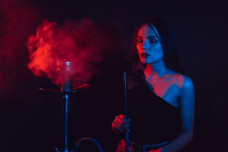 Model girl smokes hookah, sheesha. The girl exhales with pleasure. Color lightの写真素材