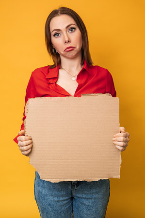 A beautiful positive young Caucasian woman is holding an empty banner on a yellow background. Copying space.の写真素材