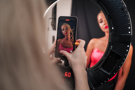 Shooting for social networks, an insider girl shoots an image made by a makeup artist and a hairdresser. Promotion in social networks. networks. Focus on the phone.の写真素材