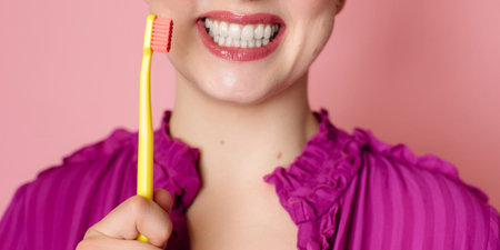 Close-up of a womans snow-white smile. Next to it is a toothbrush in a womans hand. panoramic banner.の写真素材