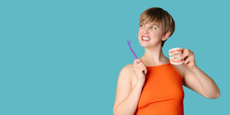 A young white woman with an amazing smile, a toothbrush and a jaw model in her hands on a blue...