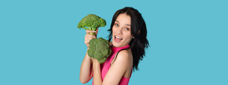 Caucasian young woman holding fresh broccoli on a blue background. Panorama, a place for textの写真素材